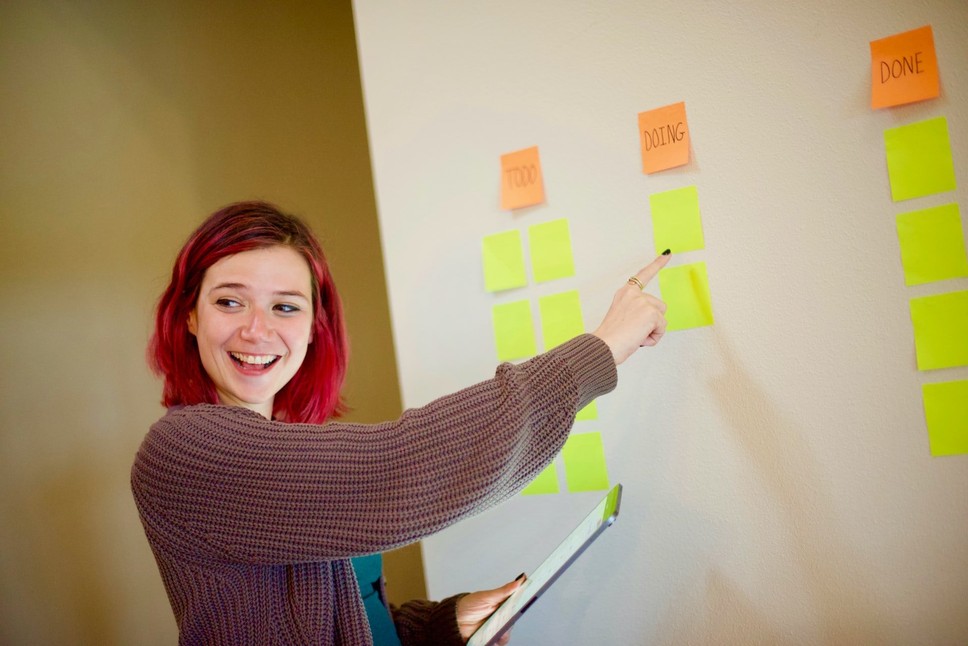 Hands placing a yellow sticky note on a glass board of colorful notes.
